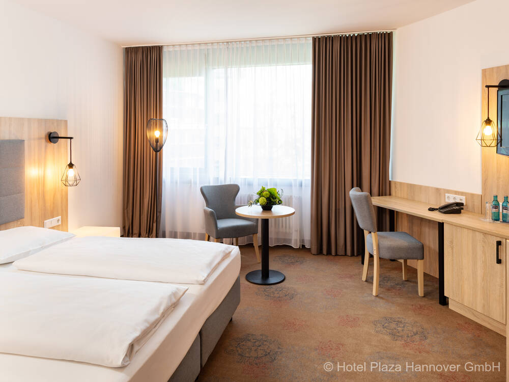 Modern eingerichtetes Hotelzimmer mit Queensizebett, Sitzecke am Fenster und großzügigem Schreibtisch mit Flachbild-TV.